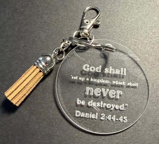 A clear acrylic keychain with a brown tassel and lobster claw, featuring a round disc engraved with the Bible verse 'God shall set up a kingdom, which shall never be destroyed. Daniel 2:44-45'.