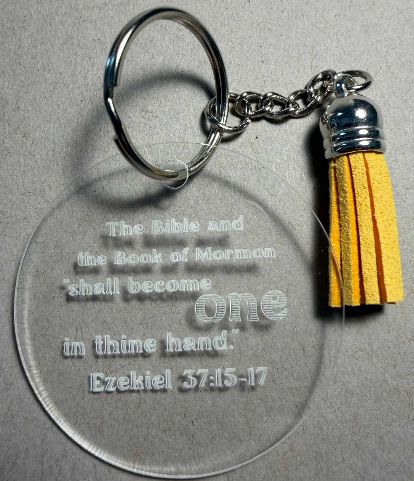A clear acrylic keychain with a silver split ring and tassel, featuring the engraved text 'God shall set up a kingdom, which shall never be destroyed. Daniel 2:44-45' on a textured gray background.
