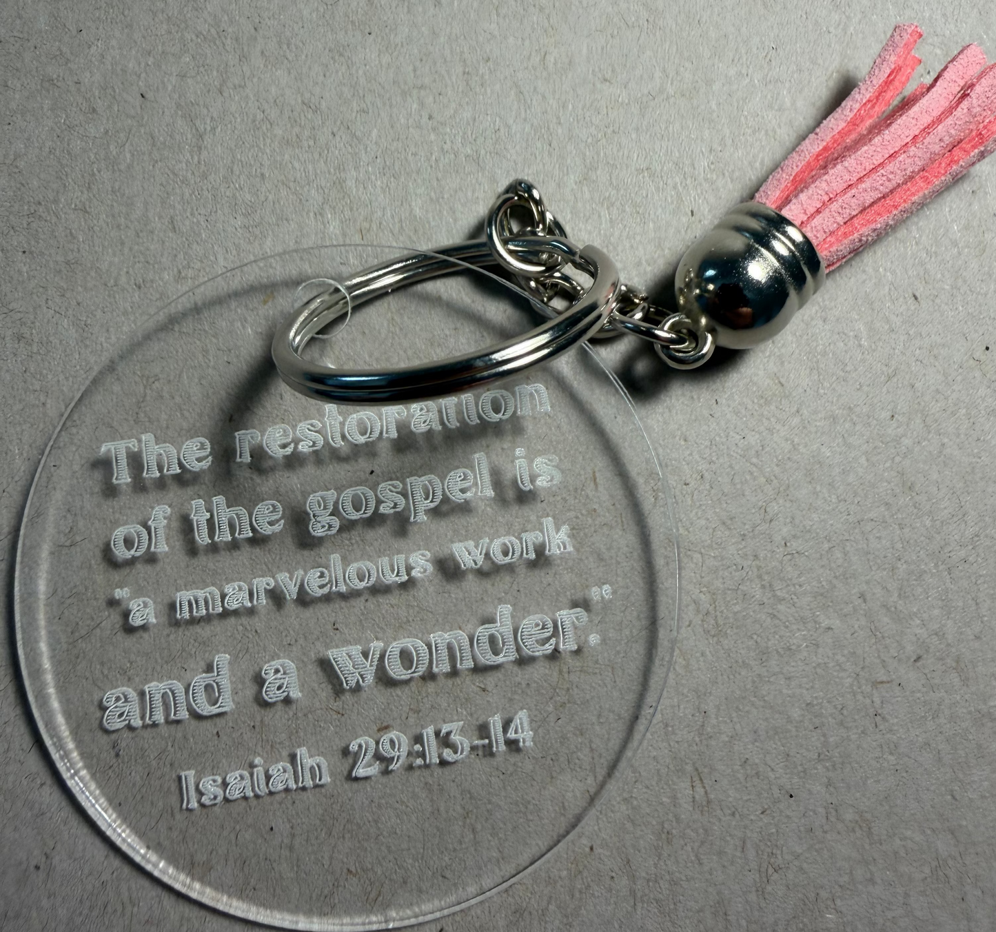 A clear acrylic keychain featuring a silver metal split ring and a bright blue tassel. The round clear acrylic disc is engraved with the Bible verse, 'Surely [Jesus Christ] hath borne our griefs, & carried our sorrows.