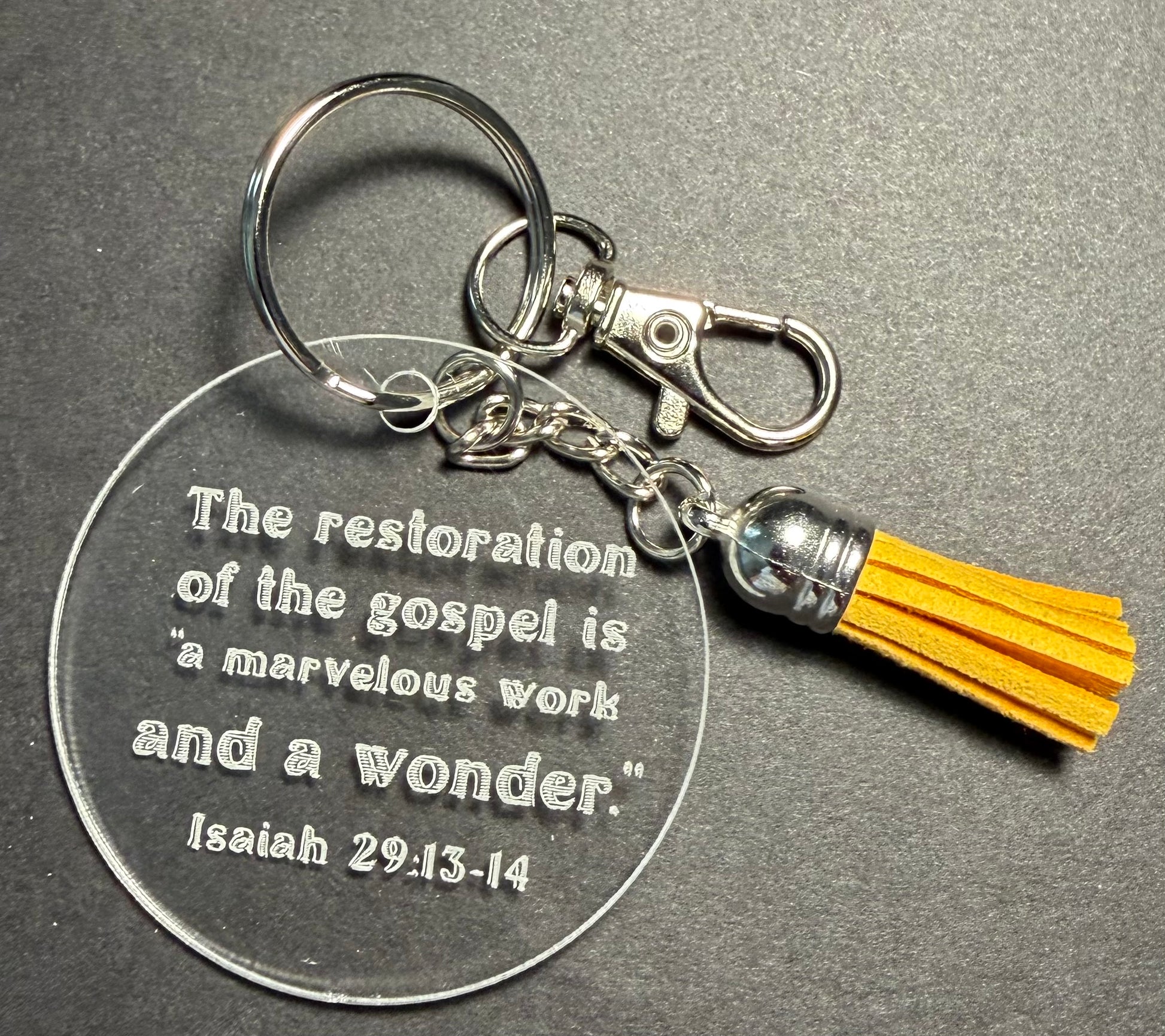 A clear acrylic keychain with an engraved Bible verse from Isaiah 29:13-14, attached to a silver-tone metal clasp and key ring, and finished with a yellow tassel charm on a dark gray background.