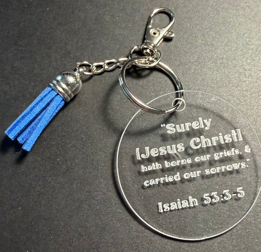 A clear acrylic keychain with a blue tassel and silver metal hardware, featuring an engraved Bible verse from Isaiah 53:3-5 on a dark gray background.