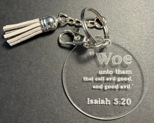 A clear acrylic keychain with a silver-tone metal clasp, split ring, and tassel. The round clear disc is engraved with the quote: 'Woe unto them that call evil good, and good evil.