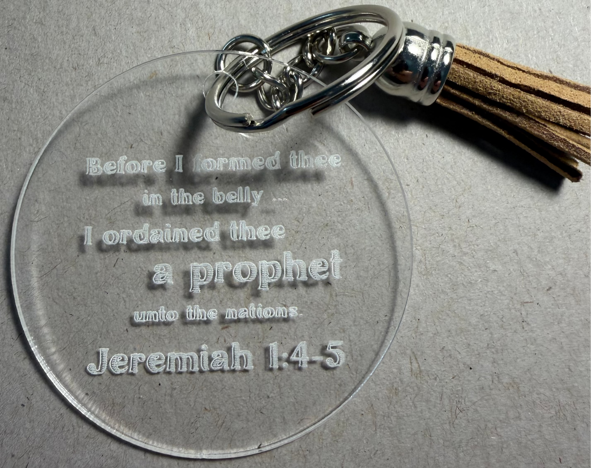 A clear acrylic keychain with engraved text reading 'Before I formed thee in the belly.