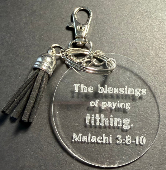 A clear acrylic keychain with a silver lobster clasp, split ring, and black tassel. The round clear acrylic disc is engraved with the text 'The blessings of paying tithing.