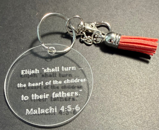 A clear acrylic keychain with an engraved Bible verse from Malachi 4:5-6, attached to a silver metal split ring and clasp, and finished with a coral  tassel, shown on a dark gray background.